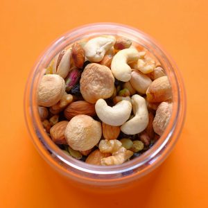 Close-up of a mix of nuts in a clear container against an orange background.