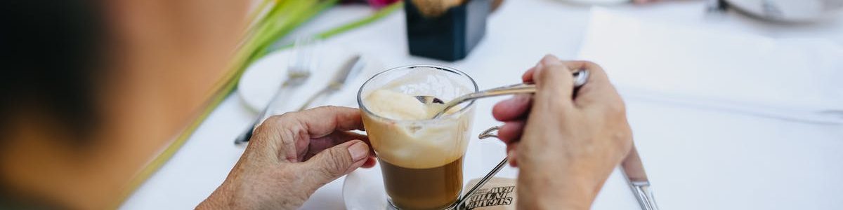 Senior couple stirring coffee at an outdoor cafe. Bright flower decor adds a cheerful touch.